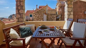A terrace with a wooden table and chairs, a stone wall, and a view of buildings with red roofs. - Hedera Estate, Hedera A22 (Dubrovnik)
