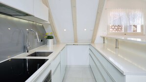 A modern kitchen with a black stove, stainless steel sink, and white cabinetry. - Hedera Estate, Hedera A22 (Dubrovnik)