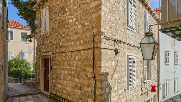 A stone building with a wooden balcony, a red door, and a staircase leading to the entrance. - Hedera Estate, Hedera A22 (Dubrovnik)