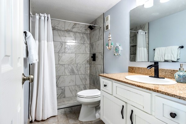 A bathroom with a shower, toilet, and vanity with a sink and mirror.