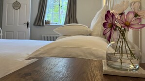 A bedroom with a bed, a bedside table with a vase of flowers, a window with curtains, and a wall-mounted lamp. - The Coach House at Lackington Farm (Dorchester)