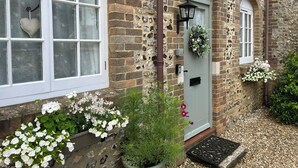 A stone building with a white door, a window with a heart-shaped hole, and a flower box with white flowers. - The Coach House at Lackington Farm (Dorchester)