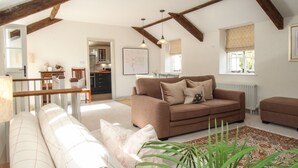 A spacious living room with a brown sofa set, a dining area with a wooden table, and a kitchen in the background. - The Coach House at Lackington Farm (Dorchester)