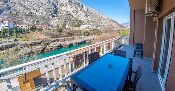 A balcony with a table and chairs overlooking a river and mountains.