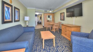 Habitación de hotel con un sofá azul estampado, una mesa de madera, un televisor y cuadros en las paredes.