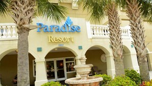 Edificio del Paradise Resort, con una señal, palmeras y una fuente al frente.