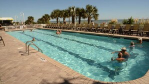 Un área de piscina con agua cristalina, sillas de descanso y palmeras.