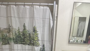 Ein Badezimmer mit Duschvorhang, der Bären und Tannenzweige zeigt, einer Toilette, einem Waschbecken und einem dunkelblauen Teppich.