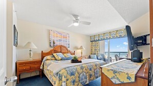 Un dormitorio con cama, mesitas de noche, escritorio, ventilador de techo, ventana con cortinas y balcón.