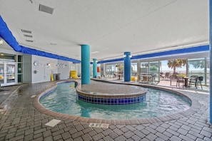 An indoor swimming pool with a tiled edge, blue pillars, and a brick floor.