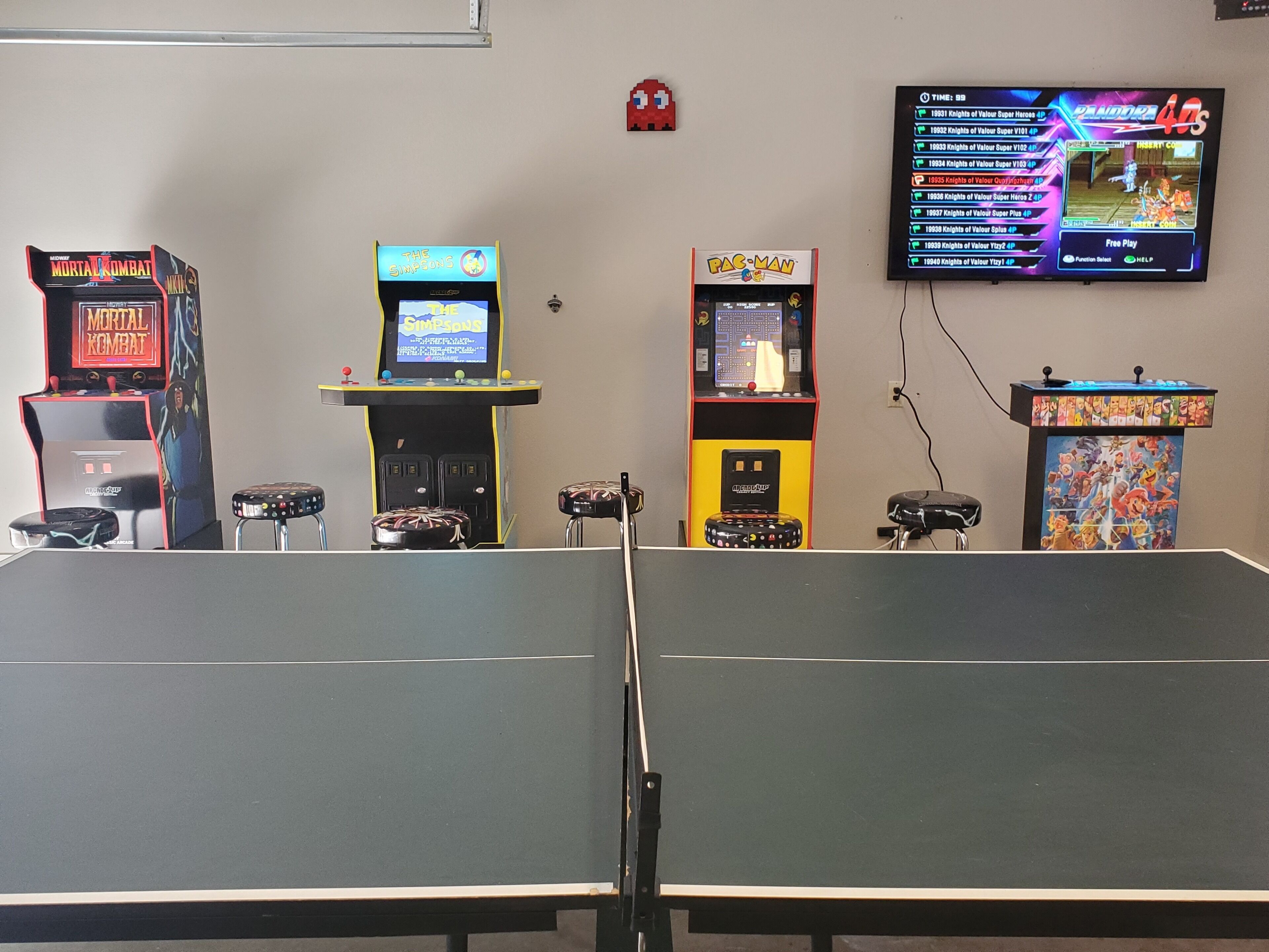 Une salle avec une table de ping-pong, des jeux d’arcade, notamment Mortal Kombat, Les Simpson et Pac-Man, et un téléviseur affichant un menu de jeux.