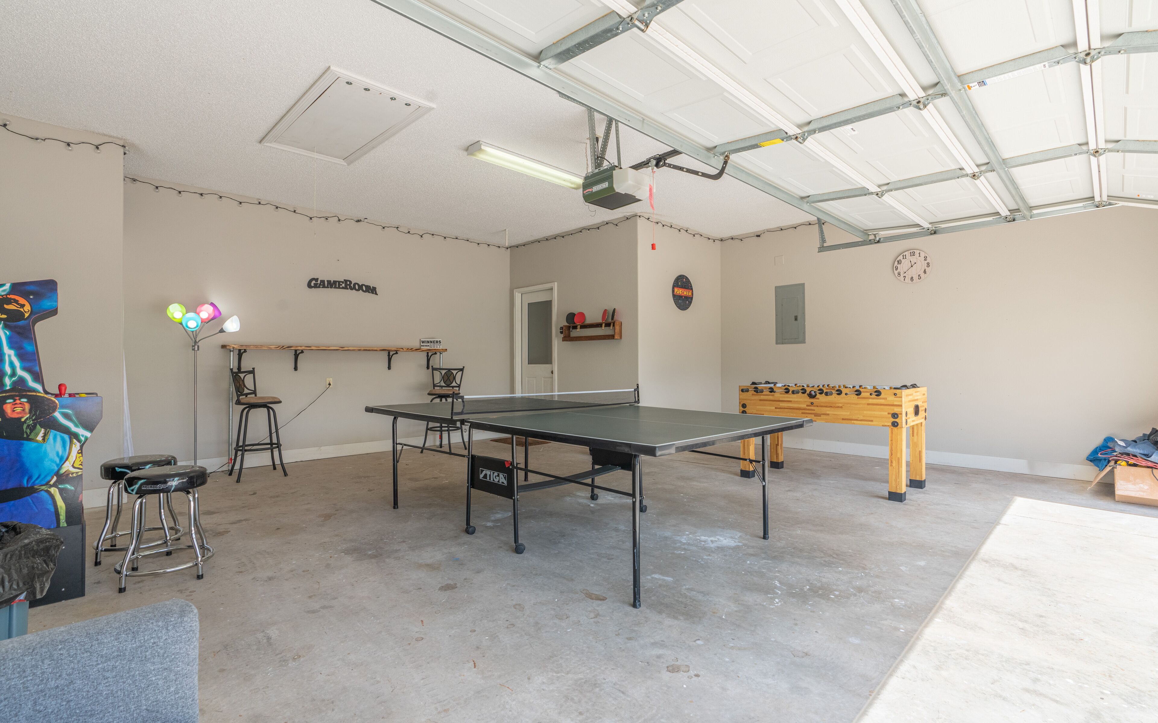 Ett rymligt inomhusområde med ett bordtennisbord, ett fotbollsspel och en spelhörna med pallar och en skylt med texten ”Vinnare”.
