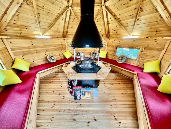A cozy cabin interior with a central fireplace, wooden walls, and red cushioned seating.