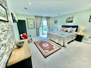 Une chambre à coucher comprenant un lit, des tables de chevet, un bureau, une chaise, un tapis et une vue sur l’extérieur.