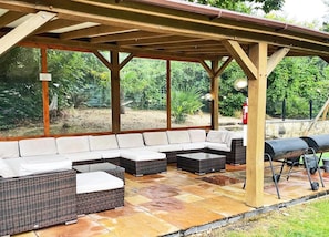 A covered outdoor seating area with a sectional sofa, two side tables, and a barbecue grill. - Osmund House Salisbury (Salisbury)