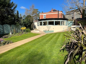 A residential property with a well-maintained lawn, a pathway leading to a house with a distinctive blue and white facade, and a brick chimney. - Osmund House Salisbury (Salisbury)