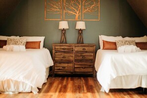 A bedroom with two beds, a wooden dresser, and wall art.