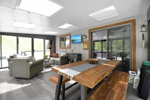 Un intérieur moderne avec une table à manger en bois, des meubles en osier et un téléviseur fixé au mur.