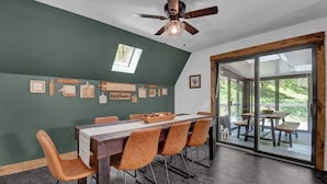 Una sala da pranzo con un lungo tavolo, diverse sedie, una ventola a soffitto e vista su un patio esterno attraverso porte in vetro.
