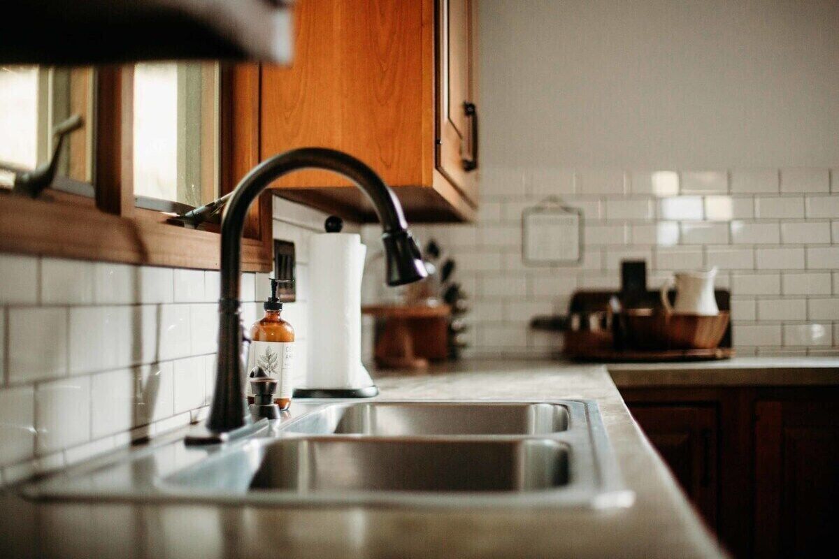 A kitchen with a stainless steel sink, wooden cabinets, and a white tiled backsplash.