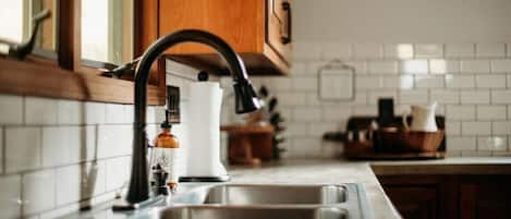 A kitchen with a stainless steel sink, wooden cabinets, and a white tiled backsplash.