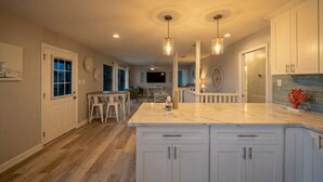 A spacious kitchen with white cabinets, a marble countertop, and pendant lighting. - Cozy Home w/ 2 Pools, Vball Court, & Ocean Views (Galveston)