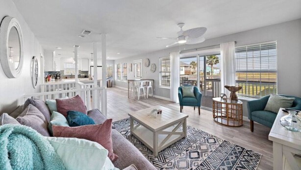 A spacious living room with a sofa, coffee table, and chairs. There is a balcony with a view of the ocean. - Cozy Home w/ 2 Pools, Vball Court, & Ocean Views (Galveston)