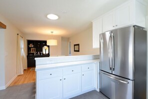 Una cocina moderna con armarios blancos, un refrigerador de acero inoxidable y una lámpara colgante.
