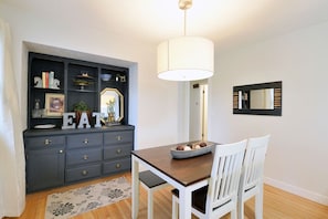 Un comedor con una mesa de madera oscura, sillas blancas, un cuenco decorativo y un espejo montado en la pared.