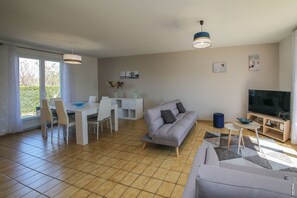 A modern living room with a grey sofa, a dining table with chairs, a TV, and a large window. - PRETTY HOUSE - GARDEN - QUIET - GAILLAC (Gaillac)