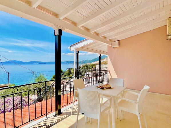 Ein Balkon mit Tisch und Stühlen, mit Blick auf ein Gewässer und Hügel.