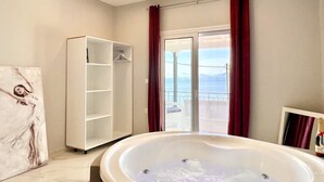 A bathroom with a bathtub, a walk-in closet, and a view through a glass door. - Nissaki Anemone Luxury Apartment with Jacuzzi (Nissaki)