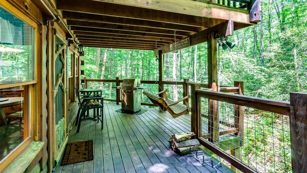 A wooden deck with a grill, chairs, and a view of the forest. - Romantic Creekside Cabin-Secluded Mountain Escape (Pigeon Forge)
