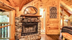A cozy cabin interior with a stone fireplace, wooden walls, and a large mirror above it. - Romantic Creekside Cabin-Secluded Mountain Escape (Pigeon Forge)