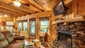 A cozy cabin interior with a stone fireplace, wooden walls, a leather sofa, and a flat-screen TV mounted above the fireplace. - Romantic Creekside Cabin-Secluded Mountain Escape (Pigeon Forge)