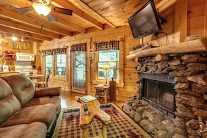 Cozy cabin interior with a leather sofa, stone fireplace, and mounted TV.
