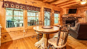 A wooden cabin interior with a dining table, chairs, a fireplace, and a television mounted on the wall. - Romantic Creekside Cabin-Secluded Mountain Escape (Pigeon Forge)