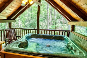 Relax in a hot tub surrounded by lush greenery and a wooden cabin.