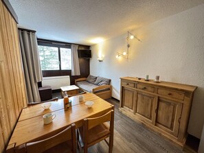 Cozy room with a dining table for two, kitchenette, and large window.