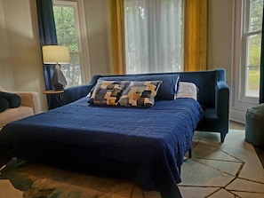 Un dormitorio con una cama grande, una mesita de noche, una lámpara y vistas a la vegetación exterior.