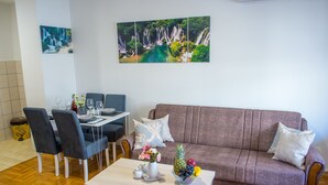 Een woonkamer met een bank, stoelen, een eettafel en een schilderij van een waterval.