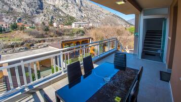 Un balcon avec une table et des chaises, donnant sur un paysage montagneux avec des bâtiments visibles au loin.