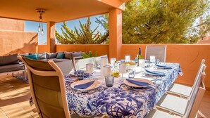 Un área de comedor al aire libre con una mesa preparada para cuatro personas, rodeada de paredes anaranjadas y vistas a árboles.