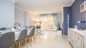 Un área de comedor moderna con una mesa dispuesta para cuatro personas, un sofá y un televisor sobre un mueble.