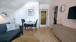 A modern living room with a grey sofa, a dining table with two chairs, a wooden cabinet, and a TV mounted on the wall. - Vacation apartment Edeltraud on Lake Millstatt, hiking vacation and much more, apartment 3 (Radenthein)
