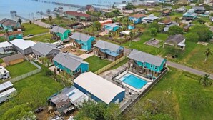 An aerial view of a residential area with houses, a swimming pool, and a pier extending into the water. - Stunning Home with Expansive Pool & Game Room (Kemah Area)