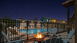 A poolside area with a fire pit, lounge chairs, and a view of a swimming pool under a starry night sky. - Stunning Home with Expansive Pool & Game Room (Kemah Area)