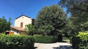 Un edificio a due piani con tetto in tegole, immerso nel verde e con un vialetto sterrato che conduce a un ingresso coperto.