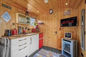 Interior de una cabaña de madera con área de cocina, un reloj, un letrero de Netflix y un cartel de bienvenida a Railway View por Blue Puffin Stays.
