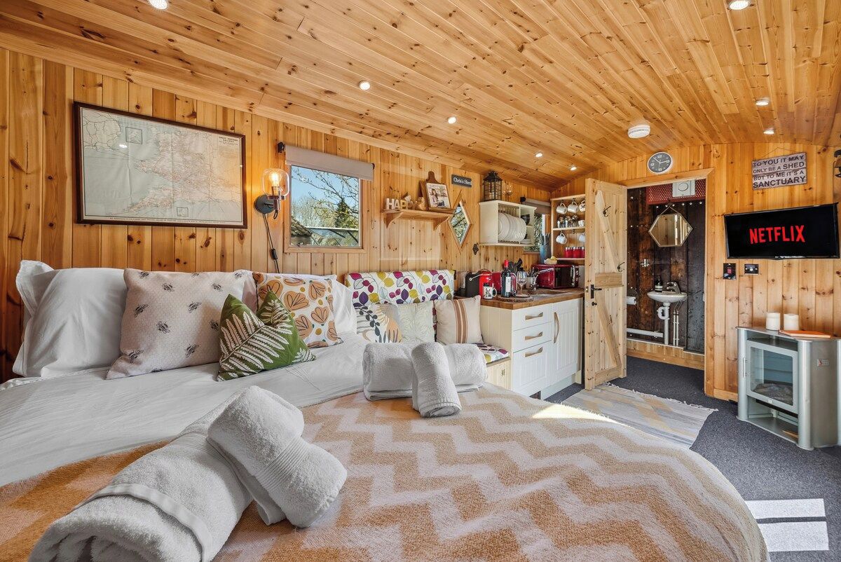 A cozy wooden room with a bed, a map on the wall, a kitchen area, and a Netflix sign.